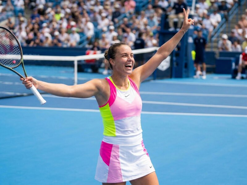 Iga Swiatek célèbre sa victoire sur le court de tennis avec une raquette à la main et le signe de la victoire.