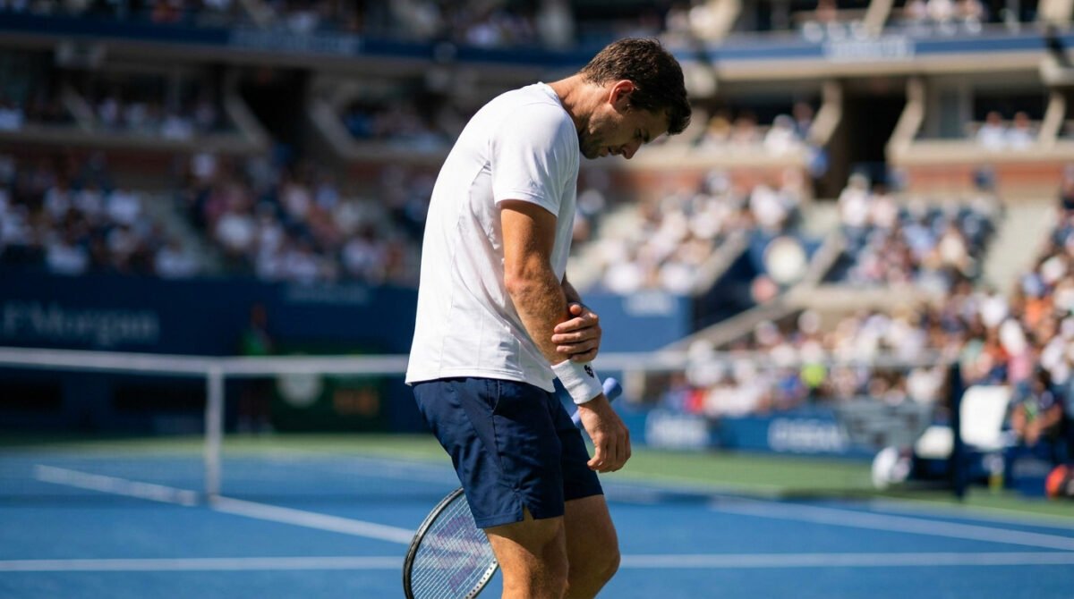 Corentin Moutet sur un court de tennis, tête basse, tenant douloureusement son poignet gauche après une blessure.