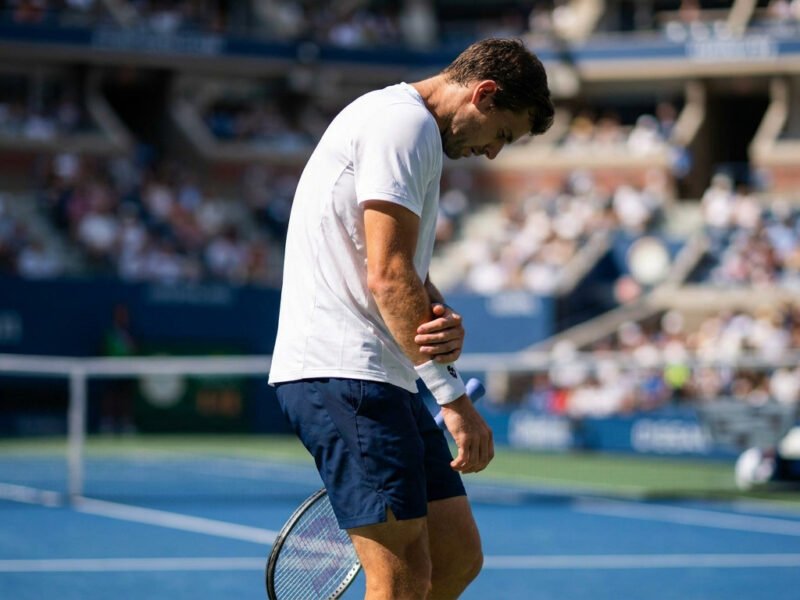 Corentin Moutet sur un court de tennis, tête basse, tenant douloureusement son poignet gauche après une blessure.